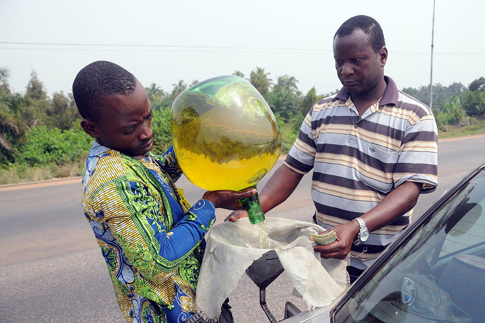 Driver filling a vehicle with gasoline from a roadside fuel seller in Benin