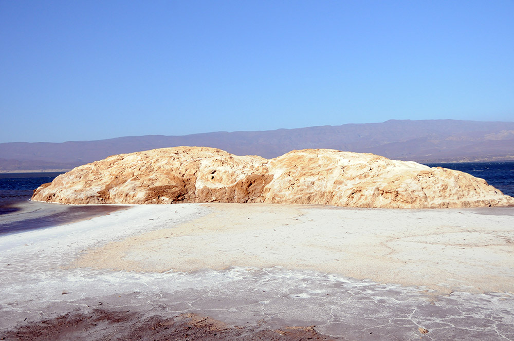 Small rocky island seen across the dry salt shoreline of Lake Assal